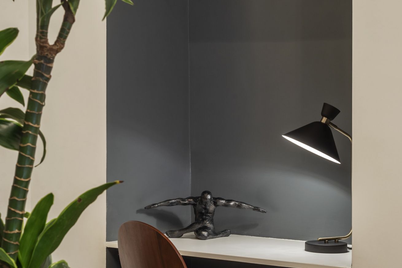 A desk with a black desk lamp, a black sculpture, and a potted plant.