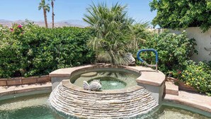 A circular pool with a central fountain and a palm tree.