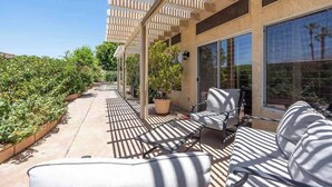A covered outdoor seating area with a pergola, potted plants, and a view of a garden.