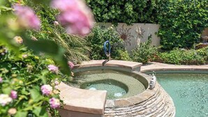 A circular hot tub with a stone edge, surrounded by lush greenery and a decorative wall with a sun motif.