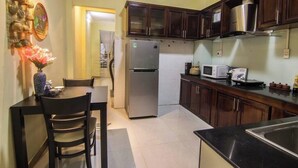 A compact kitchen with dark wooden cabinets, a stainless steel refrigerator, a microwave, and a sink. - Moonie House Saigon (Ho Chi Minh City)