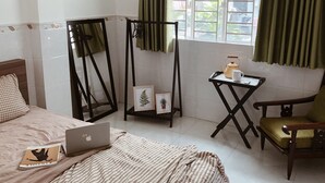 A bedroom with a bed, a laptop, a chair, a small table with a teapot and cup, and a window with curtains. - Moonie House Saigon (Ho Chi Minh City)