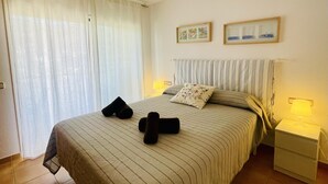 Cama bem arrumada com roupa de cama listrada, dois travesseiros e duas toalhas enroladas. Há duas mesas de cabeceira com abajures e duas fotos emolduradas na parede.