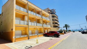 Um edifício com várias andares e varandas, um carro vermelho estacionado na frente, e um céu azul límpido.