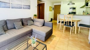 Uma sala de estar moderna com um sofá seccional cinza, uma mesa de centro com uma planta, e uma área de jantar com cadeiras de madeira e uma mesa.