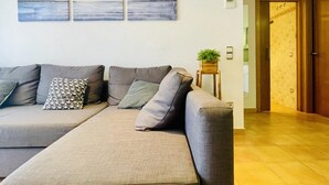 Uma sala de estar moderna com um sofá cinza, almofadas estampadas e uma pequena mesa de madeira com uma planta.