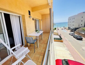 A balcony with a table and chairs, a view of the street and sea, and a building with a sign. - Voramar by Costabravaway (Sant Antoni de calonge)