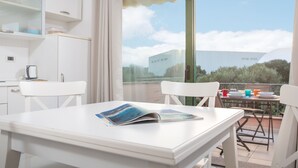 Une pièce moderne avec une table blanche, des chaises et une grande fenêtre donnant sur le ciel et les bâtiments lointains.