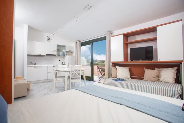 A modern hotel room with a bed, a TV, a dining area, and a balcony with a view.