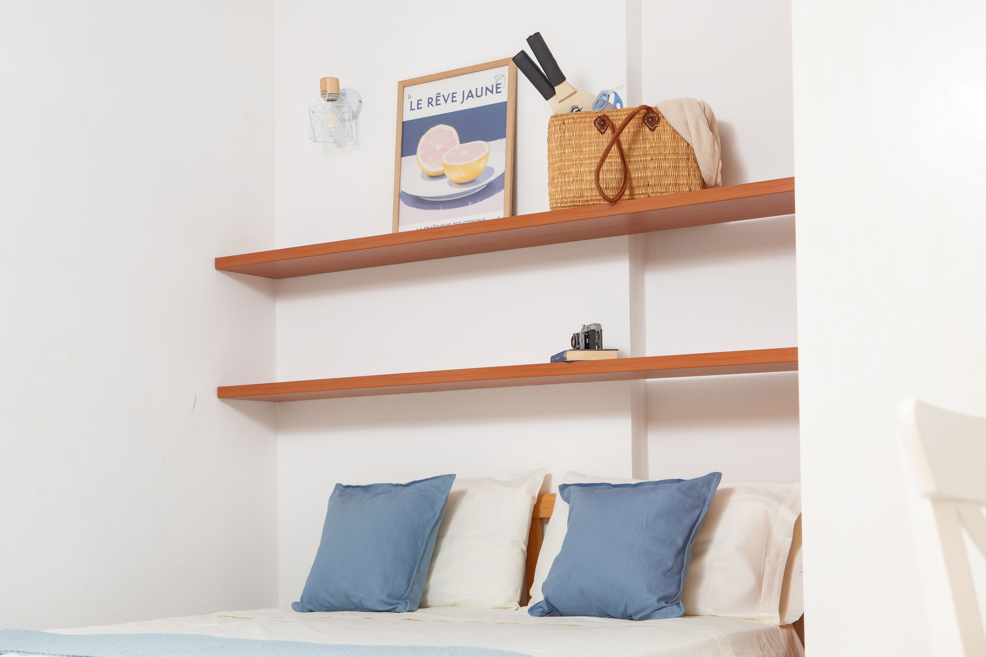Ein Schlafzimmer mit zwei Holzregalen, einem Bett mit blauen Kissen und einem Poster an der Wand.
