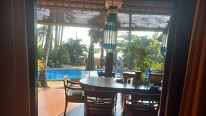 A view of a poolside area with a table and chairs, surrounded by potted plants and palm trees. - Bali North Beach Villa (Kubu)