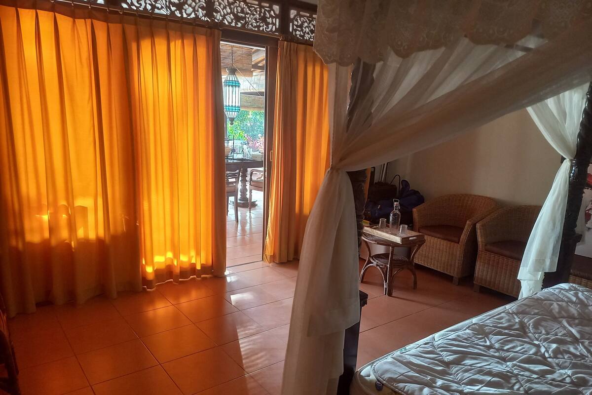 Quarto com uma cama, uma mesa com uma garrafa e copos, e uma cadeira.