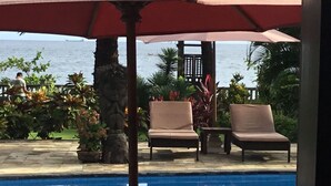 A poolside area with lounge chairs and an umbrella, overlooking a body of water. - Bali North Beach Villa (Kubu)