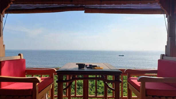 An outdoor seating area with a table and chairs, overlooking a calm sea with a boat in the distance. - Bali North Beach Villa (Kubu)