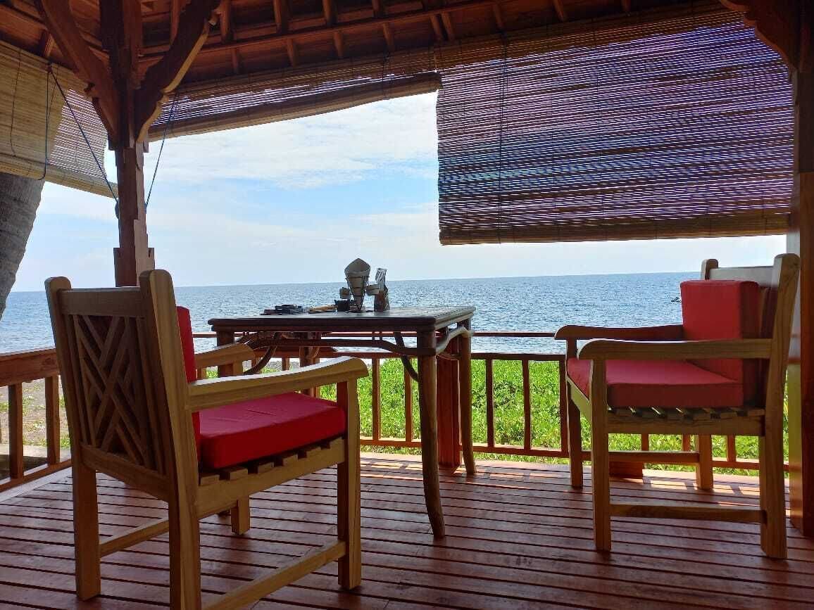 A wooden deck with a table and chairs, overlooking the sea.