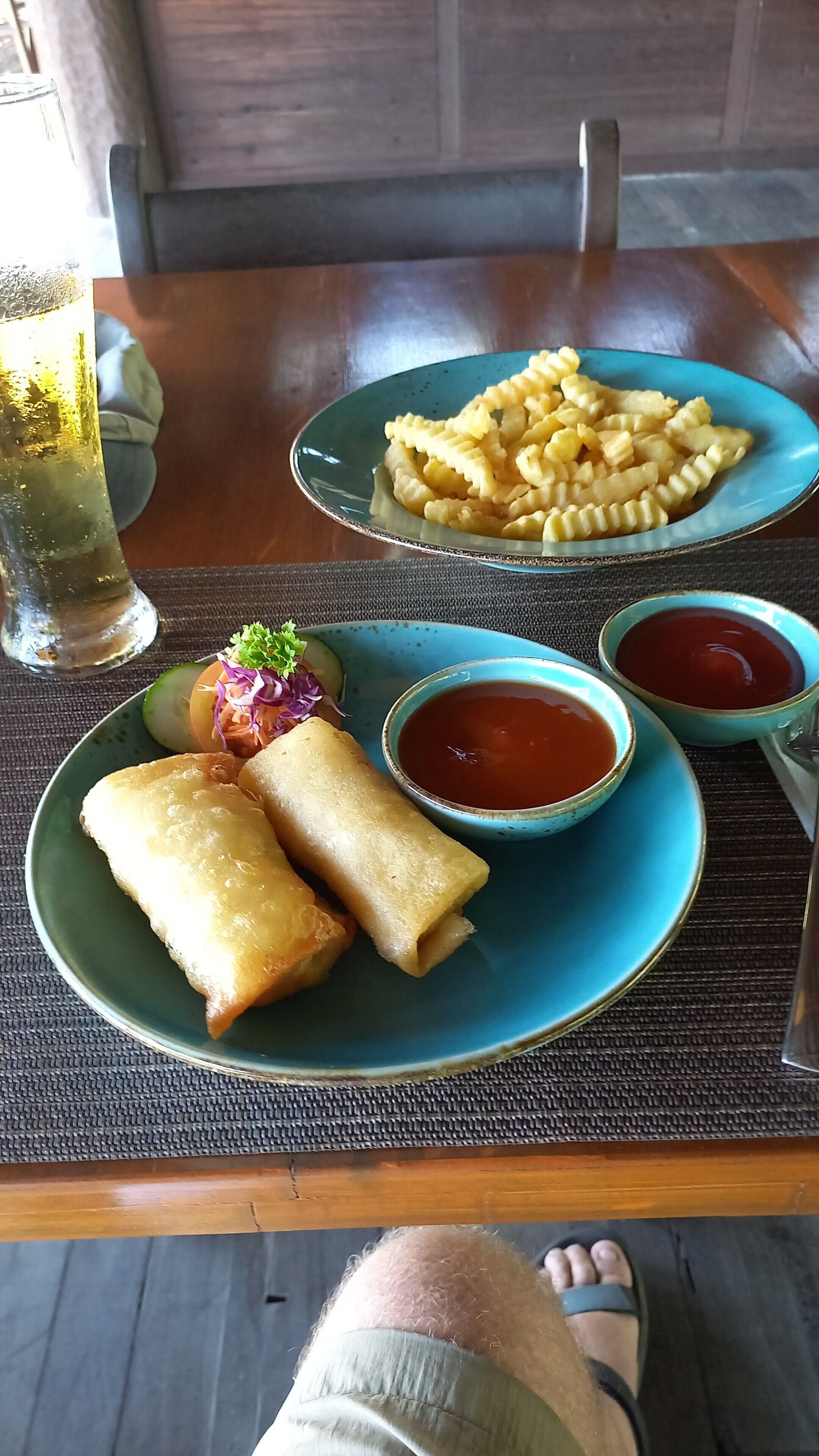 Una mesa con dos platos de comida, uno con rollitos primavera y otro con pasta, y dos cuencos pequeños de salsa.