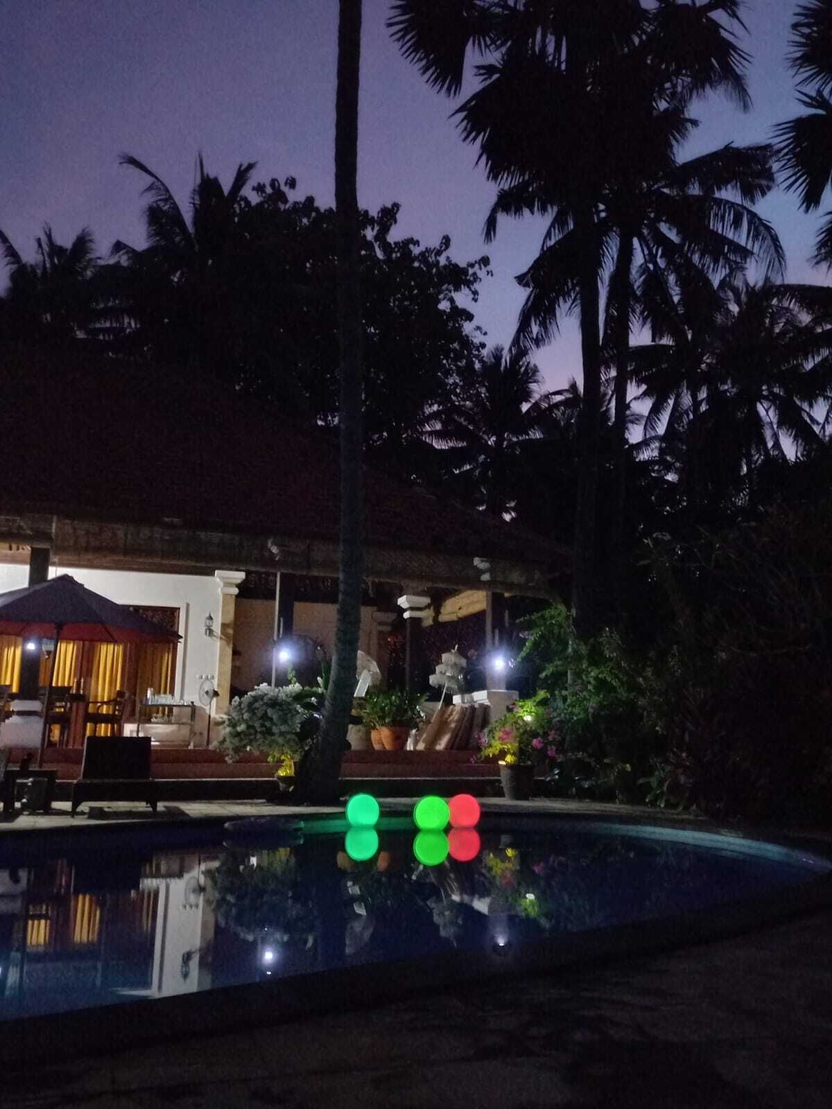 A nighttime view of a pool area with palm trees and a building with a covered seating area.