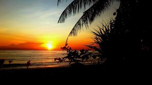A sunset over a beach with palm trees and a few people in the foreground. - Bali North Beach Villa (Kubu)