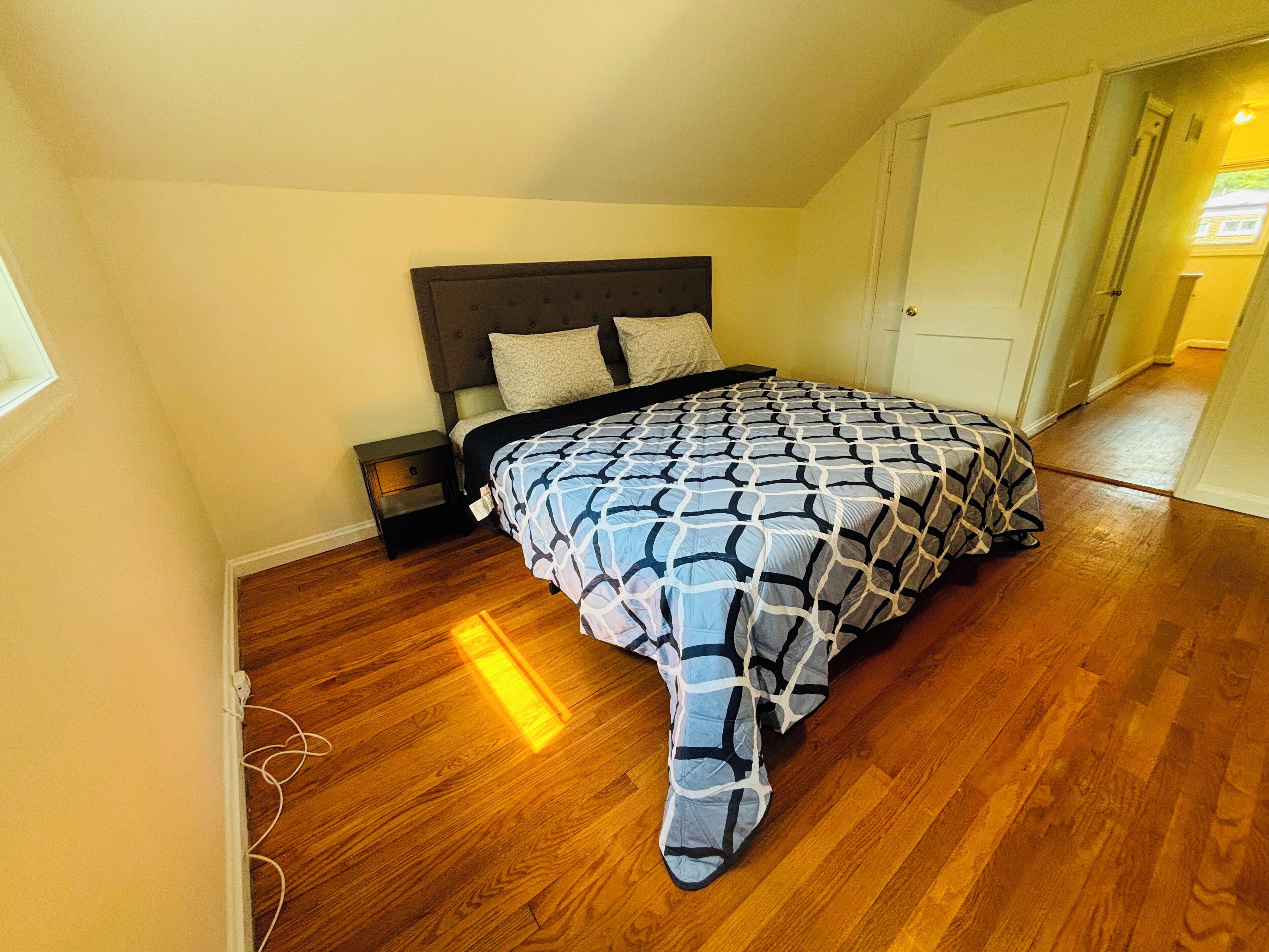 A bedroom with a bed, wooden flooring, a nightstand, and a door.