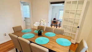Une salle à manger avec une table en bois, six chaises et un arrangement floral décoratif composé d’orchidées.