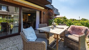 Eine Terrasse im Freien mit Korbmöbeln, einem Tisch und Blick auf ein Gebäude mit einem Balkon.