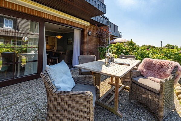 An outdoor patio with wicker furniture, a table, and a view of a building with a balcony.