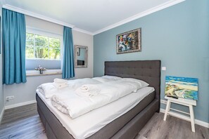 A bedroom with a large bed, a window with curtains, and two paintings on the wall.