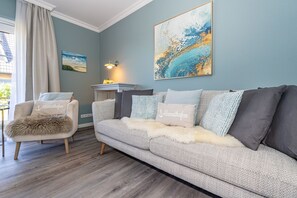A living room with a sofa, a chair with a fur throw, a painting, and a lamp.