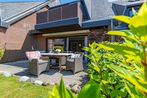 A patio with a table and chairs, a brick wall, and a garden with plants and rocks. - Nis Puk - vacation apartment in Westerland for max. 3 persons, with west-facing terrace and (Sylt)