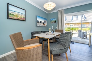 A dining area with wicker chairs, a table, and artwork on the walls. - Nis Puk - vacation apartment in Westerland for max. 3 persons, with west-facing terrace and (Sylt)