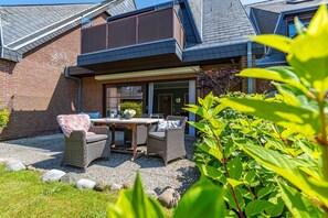 A patio with a table and chairs, a brick wall, and a garden with plants and rocks.