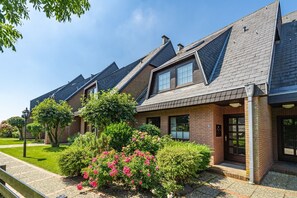 A row of modern houses with pitched roofs and brick exteriors, surrounded by well-maintained gardens and a clear sky.