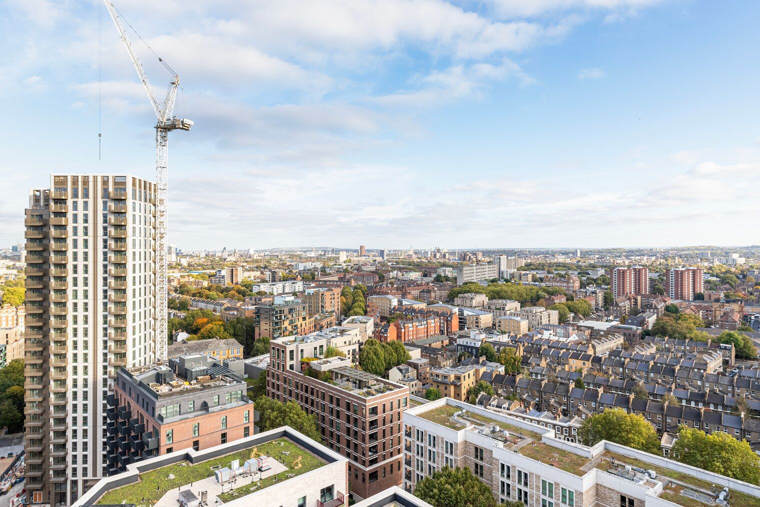 Un immeuble de grande hauteur, avec une grue de construction, entouré d’un quartier urbain dense, composé de différents bâtiments, et sous un ciel dégagé.