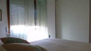 A bedroom with a bed, two pillows, a window with blinds, and a door.