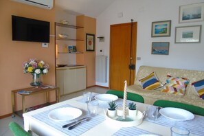 Een eethoek met een tafel voor vier personen, een aan de muur bevestigde televisie en een bank met kleurrijke kussens.