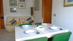 A dining area with a table set for two, a sofa with colorful cushions, and framed artwork on the wall.