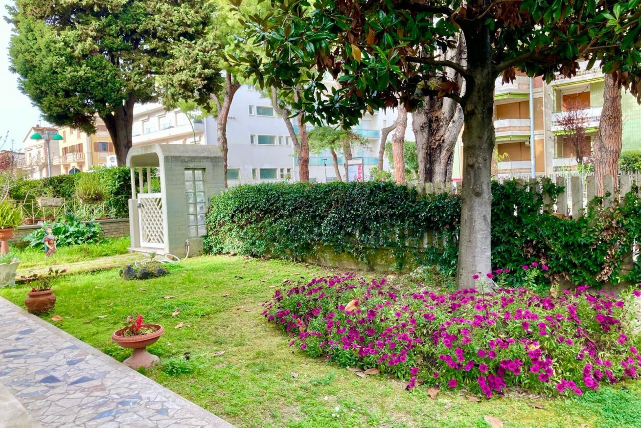 A well-maintained garden with a variety of plants and flowers, a paved pathway, and a building with multiple balconies in the background.