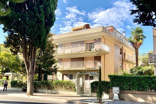 A multi-story building with balconies, a gated entrance, and a clear sky.