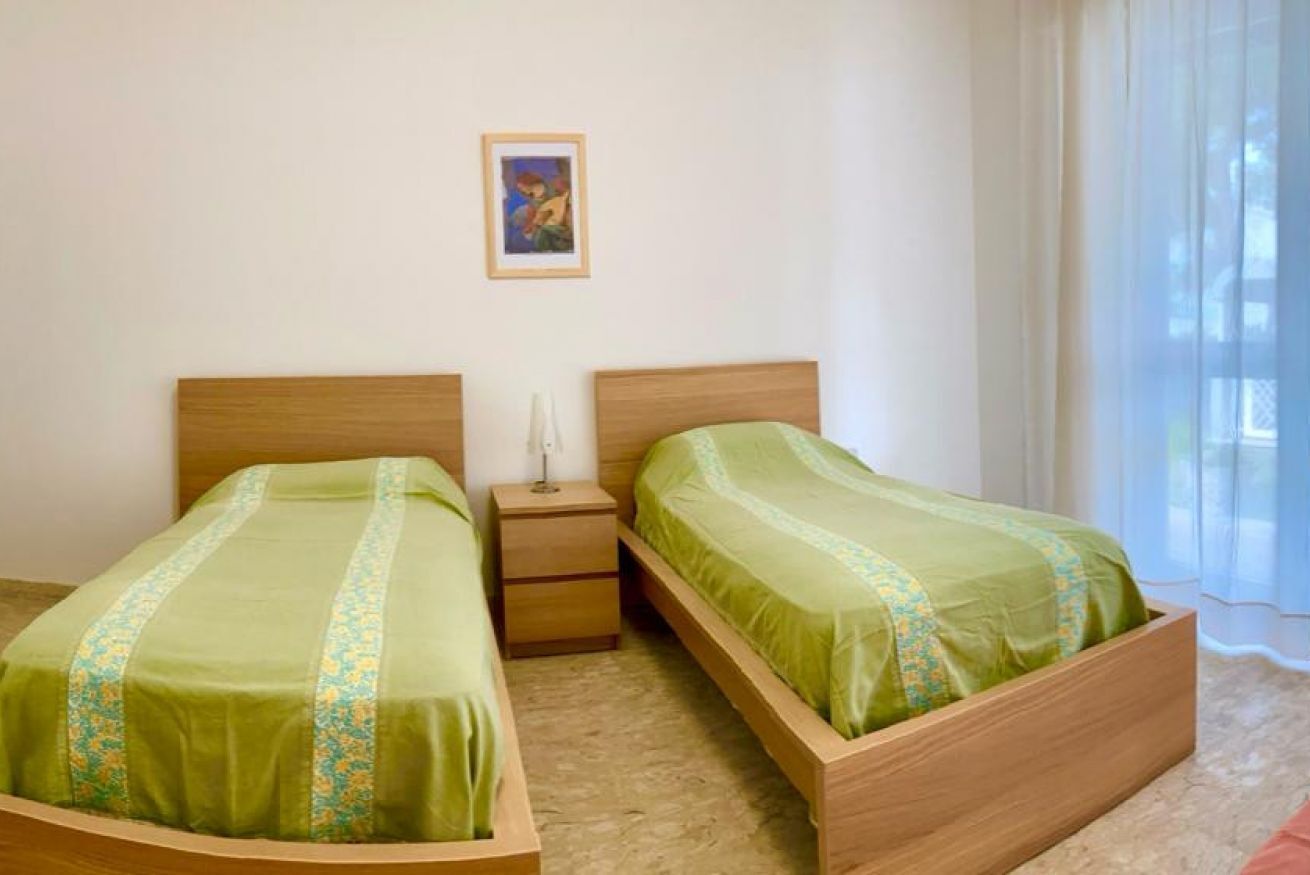 A room with two wooden beds, each with a green bedspread and a small bedside table with a lamp.