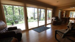A spacious living room with a large sliding glass door leading to a patio, a leather sofa, a recliner, and a dining area with chairs. - Grand Oaks Lake House (Green Lake)