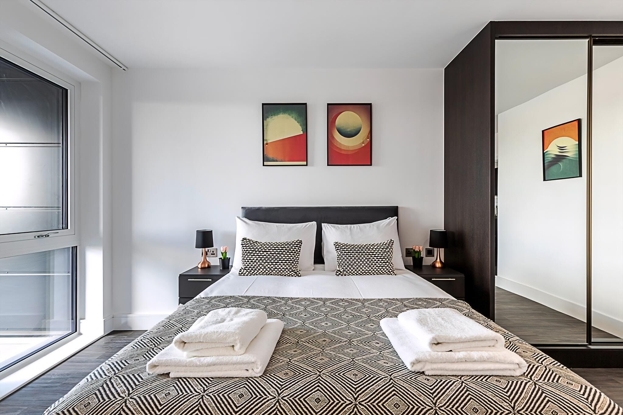 Una camera da letto moderna con un letto grande, due comodini e arte astratta appesa al muro.