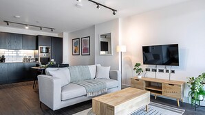 Un soggiorno moderno con un divano grigio, un tavolino in legno e una TV a parete.