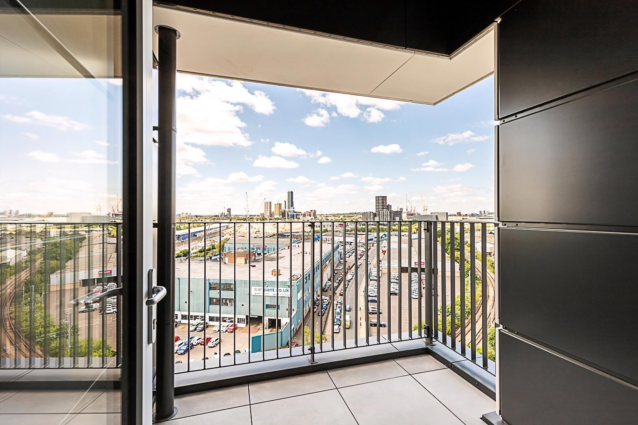 A balcony with a city view, metal railing, and a glass door.