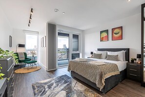 A modern bedroom with a large bed, a balcony, and city views. - Sky-high Apartment With Modern Decor (London)
