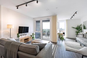 A modern living room with a sofa, TV, and a balcony with a city view. - Sky-high Apartment With Modern Decor (London)