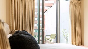 A hotel room with a bed, a window with curtains, and a view of a building outside. - Luxury Penthouse Overlooking the Thames (London)