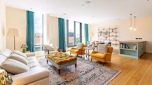 A modern living room with a sofa, ottoman, yellow armchairs, and a coffee table. There is a bookshelf and a view of the city through large windows. - Luxury Penthouse Overlooking the Thames (London)