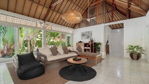 Een ruime woonkamer met een hoge plafond, een zithoek, een salontafel en een eettafel.