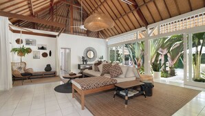Een ruime woonkamer met een hoge plafond, een groot raam en uitzicht op palmbomen.
