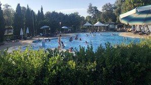 Une piscine entourée de chaises longues et de parasols, avec des arbres en arrière-plan.